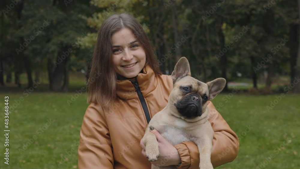 Happy woman posing at park with french bulldog on hands