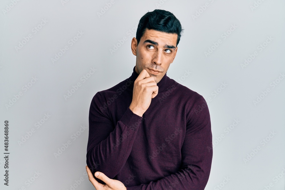Handsome hispanic man wearing turtleneck sweater thinking concentrated about doubt with finger on chin and looking up wondering Handsome hispanic man wearing turtleneck sweater thinking concentrated about doubt with finger on chin and looking up wondering