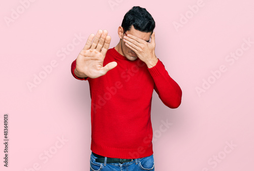 Handsome hispanic man wearing casual clothes and glasses covering eyes with hands and doing stop gesture with sad and fear expression. embarrassed and negative concept.