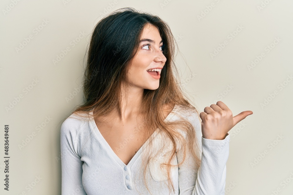 Young caucasian woman wearing casual white t shirt pointing thumb up to the side smiling happy with open mouth Young caucasian woman wearing casual white t shirt pointing thumb up to the side smiling happy with open mouth