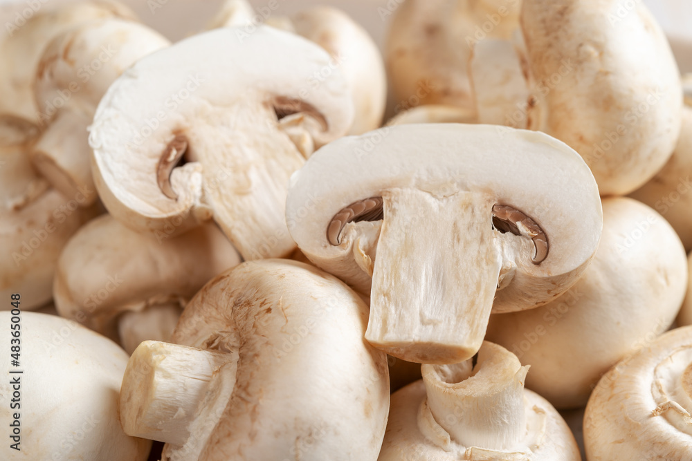 Halved raw champignon and whole button mushrooms. Cultivated white mushrooms background. Agaricus bisporus widely cultivated in the world. Vegetable protein. Vegetarian food. Dieting. Halved raw champignon and whole button mushrooms. Cultivated white mushrooms background. Agaricus bisporus widely cultivated in the world. Vegetable protein. Vegetarian food. Dieting.