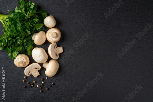 Raw champignons wole and halved and bunch of parsley over black slate slab. Cooking fresh button mushrooms Agaricus bisporus. Vegetarian menu. Recipe with vegetable protein. Copy space.
