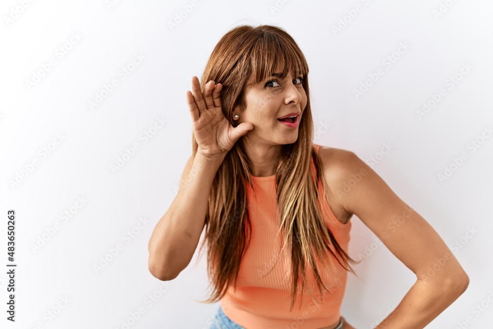 Hispanic woman with bang hairstyle standing over isolated background smiling with hand over ear listening an hearing to rumor or gossip. deafness concept. Hispanic woman with bang hairstyle standing over isolated background smiling with hand over ear listening an hearing to rumor or gossip. deafness concept.