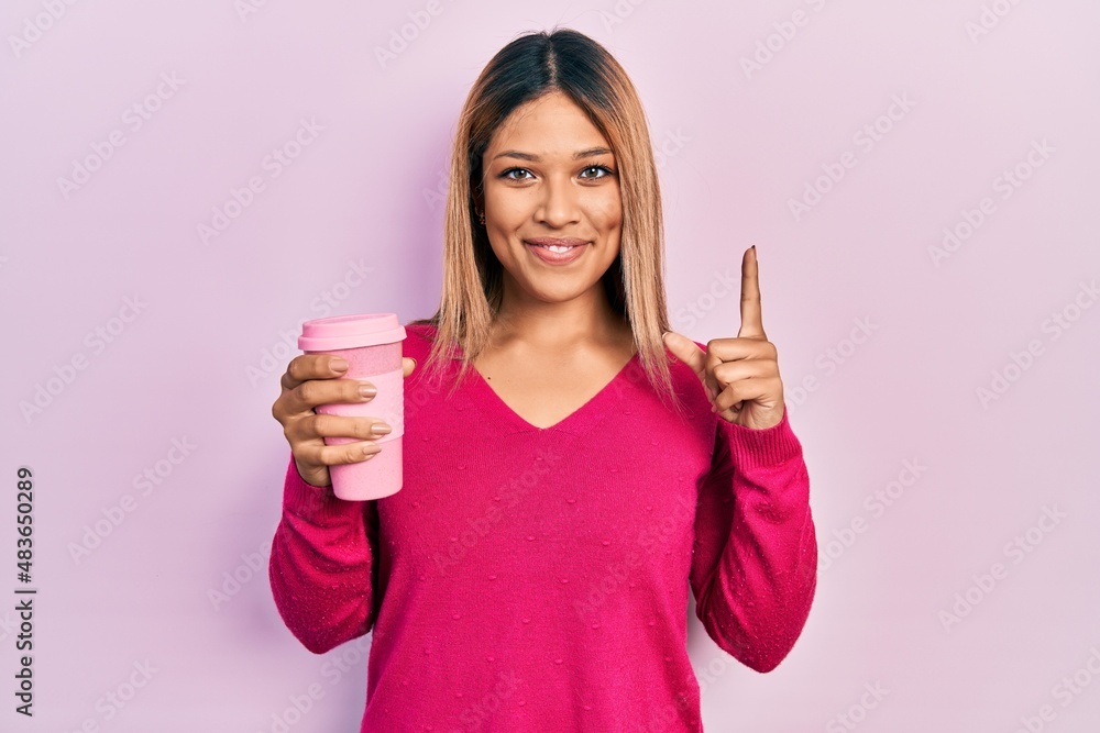 Beautiful hispanic woman drinking a take away cup of coffee smiling with an idea or question pointing finger with happy face, number one Beautiful hispanic woman drinking a take away cup of coffee smiling with an idea or question pointing finger with happy face, number one