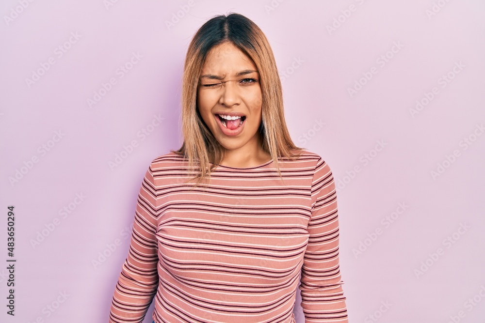 Beautiful hispanic woman wearing casual striped sweater winking looking at the camera with sexy expression, cheerful and happy face. Beautiful hispanic woman wearing casual striped sweater winking looking at the camera with sexy expression, cheerful and happy face.