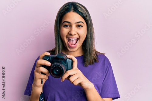 Young latin woman using reflex camera celebrating crazy and amazed for success with open eyes screaming excited.