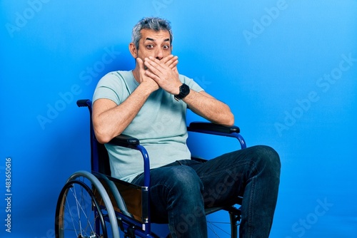 Handsome middle age man with grey hair sitting on wheelchair shocked covering mouth with hands for mistake. secret concept.
