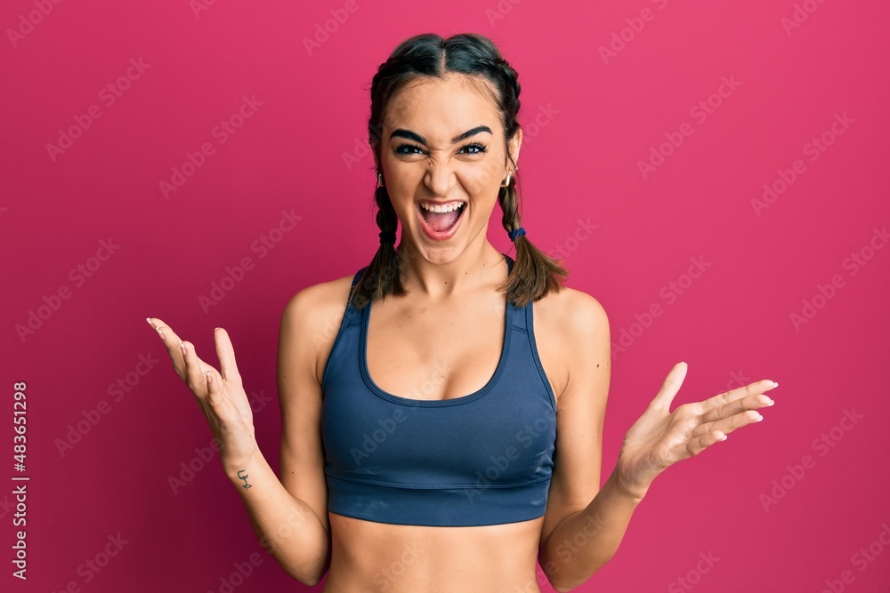 Young brunette girl wearing sportswear and braids crazy and mad shouting and yelling with aggressive expression and arms raised. frustration concept. Young brunette girl wearing sportswear and braids crazy and mad shouting and yelling with aggressive expression and arms raised. frustration concept.