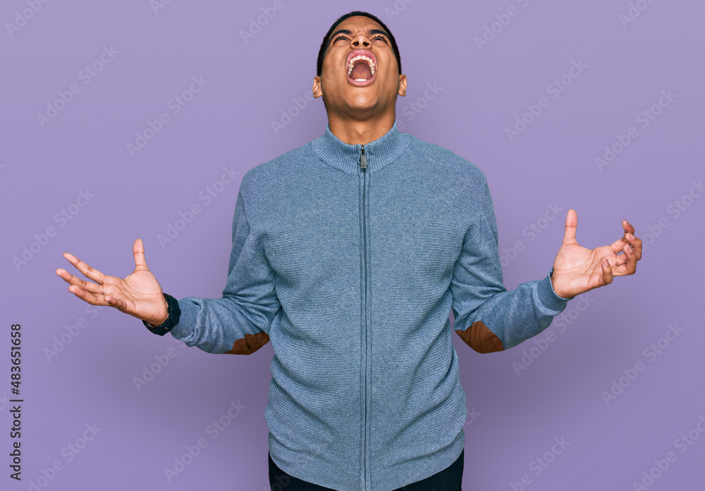 Fototapeta premium Young handsome hispanic man wearing casual sweatshirt crazy and mad shouting and yelling with aggressive expression and arms raised. frustration concept.