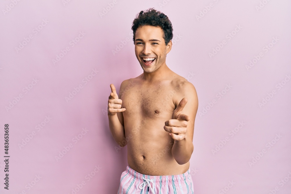 Fototapeta premium Young handsome man wearing swimwear shirtless pointing fingers to camera with happy and funny face. good energy and vibes.