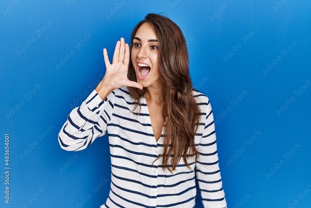 Young hispanic woman standing over blue isolated background shouting and screaming loud to side with hand on mouth. communication concept. Young hispanic woman standing over blue isolated background shouting and screaming loud to side with hand on mouth. communication concept.