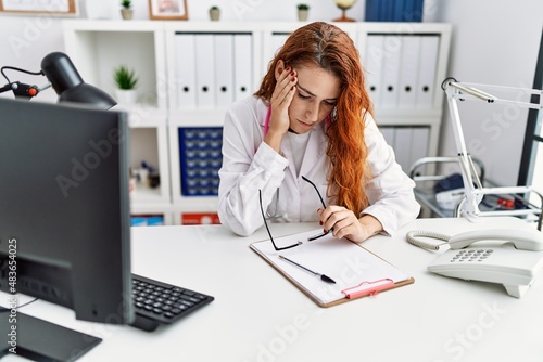 Young redhead woman wearing doctor uniform stressed at hospital