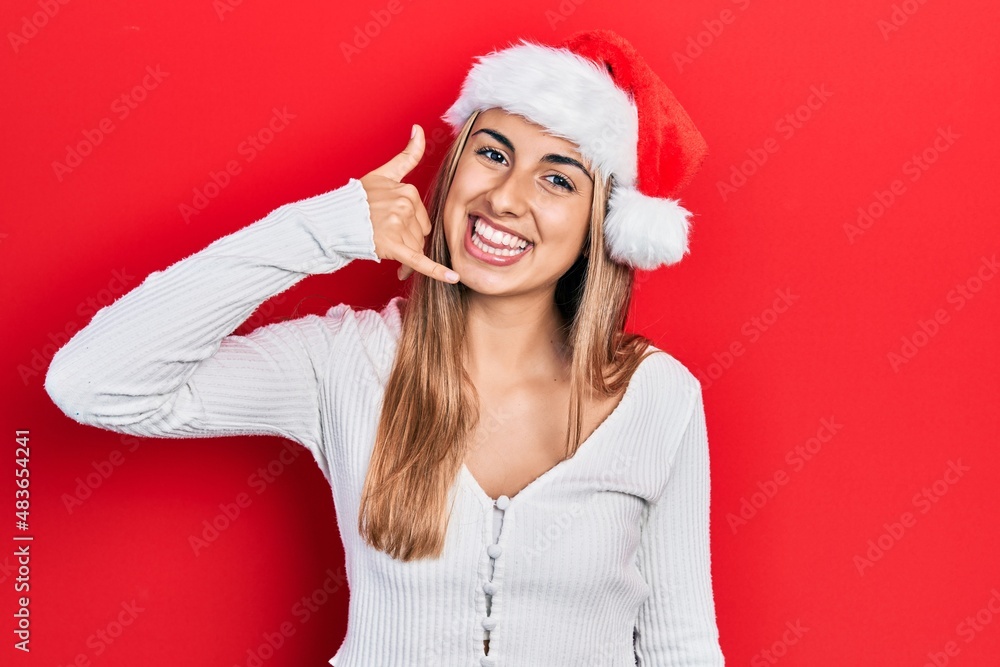 Beautiful hispanic woman wearing christmas hat smiling doing phone gesture with hand and fingers like talking on the telephone. communicating concepts. Beautiful hispanic woman wearing christmas hat smiling doing phone gesture with hand and fingers like talking on the telephone. communicating concepts.