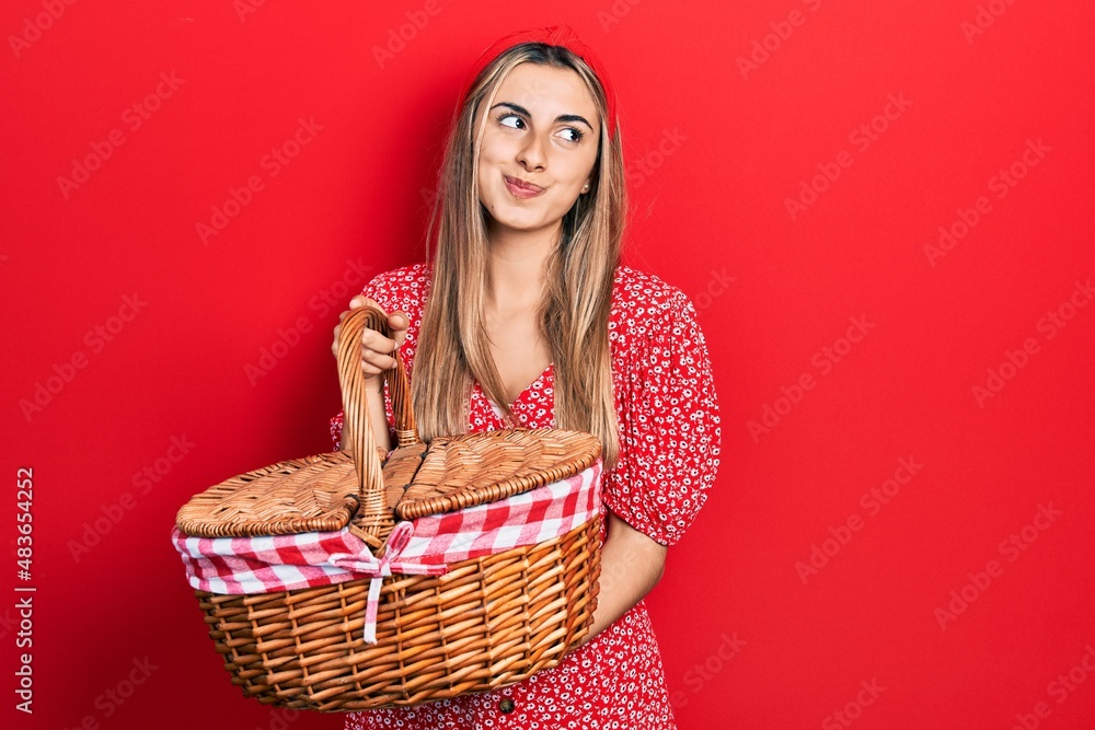 Beautiful hispanic woman holding picnic wicker basket smiling looking to the side and staring away thinking. Beautiful hispanic woman holding picnic wicker basket smiling looking to the side and staring away thinking.