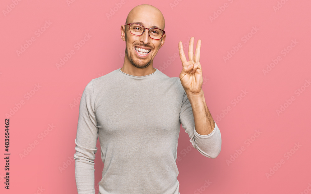 Naklejka premium Bald man with beard wearing casual clothes and glasses showing and pointing up with fingers number three while smiling confident and happy.