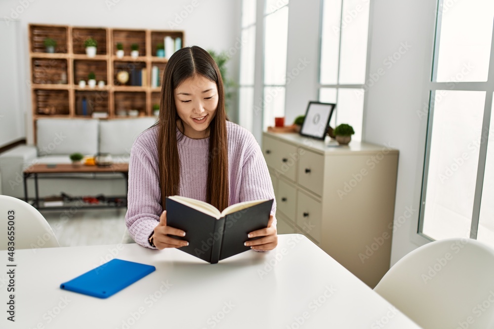 Young chinese girl reading book sitting on the table at home. Young chinese girl reading book sitting on the table at home.
