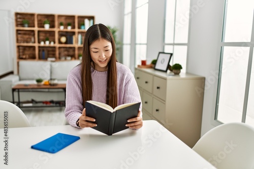 Young chinese girl reading book sitting on the table at home.