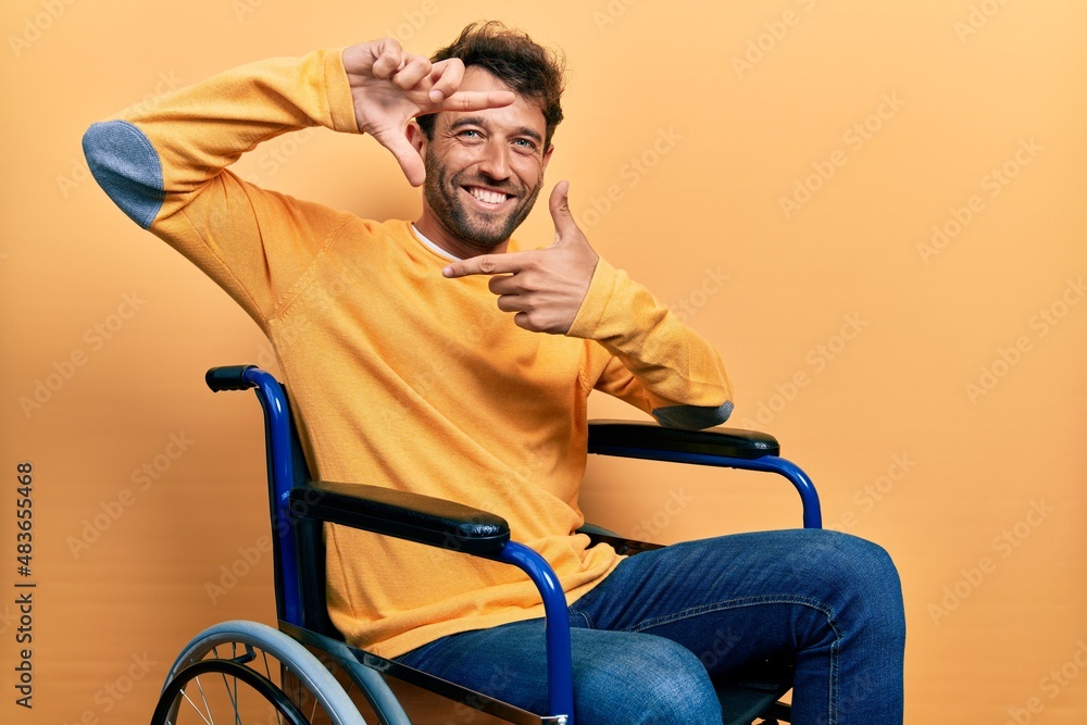 Handsome man with beard sitting on wheelchair smiling making frame with hands and fingers with happy face. creativity and photography concept. Handsome man with beard sitting on wheelchair smiling making frame with hands and fingers with happy face. creativity and photography concept.