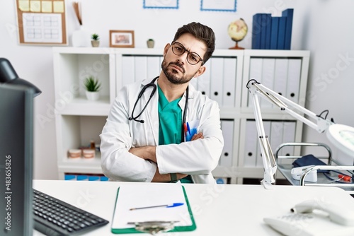 Young man with beard wearing doctor uniform and stethoscope at the clinic skeptic and nervous  disapproving expression on face with crossed arms. negative person.