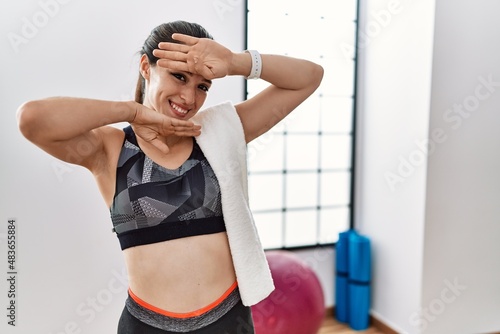 Young brunette woman wearing sportswear and towel at the gym smiling cheerful playing peek a boo with hands showing face. surprised and exited © Krakenimages.com