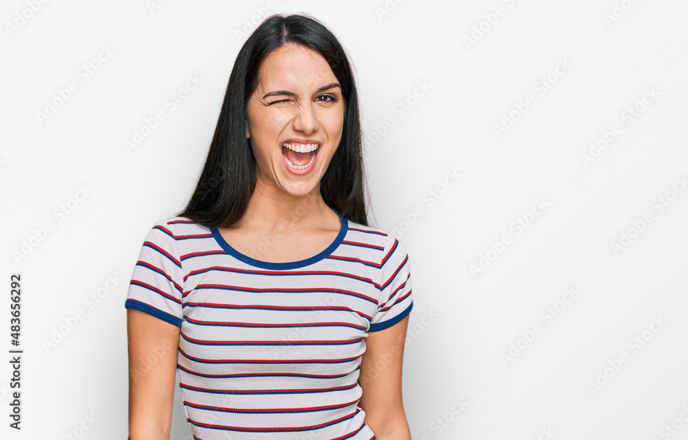 Young hispanic girl wearing casual striped t shirt winking looking at the camera with sexy expression, cheerful and happy face. Young hispanic girl wearing casual striped t shirt winking looking at the camera with sexy expression, cheerful and happy face.