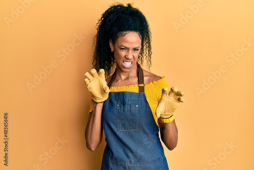 Middle age african american woman wearing professional apron smiling funny doing claw gesture as cat, aggressive and sexy expression