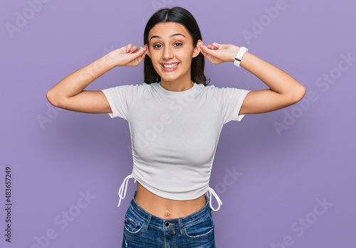 Young hispanic girl wearing casual white t shirt smiling pulling ears with fingers, funny gesture. audition problem