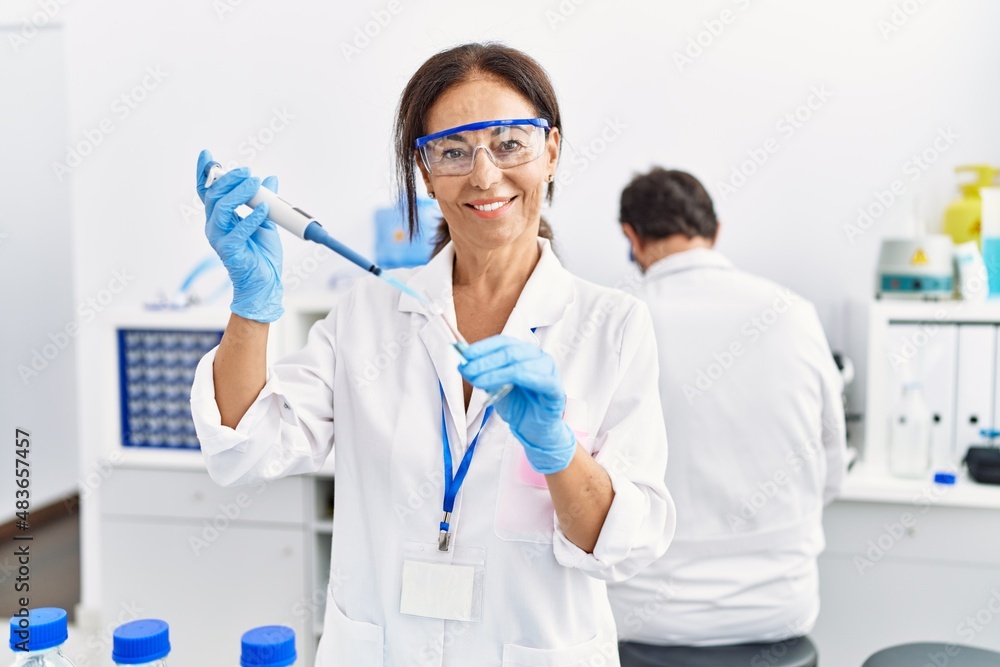Middle age man and woman partners wearing scientist uniform using pipette and test tube at laboratory Middle age man and woman partners wearing scientist uniform using pipette and test tube at laboratory