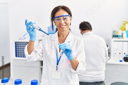 Middle age man and woman partners wearing scientist uniform using pipette and test tube at laboratory