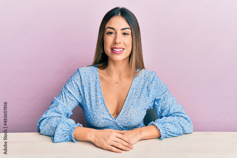 Young hispanic woman wearing casual clothes sitting on the table looking positive and happy standing and smiling with a confident smile showing teeth Young hispanic woman wearing casual clothes sitting on the table looking positive and happy standing and smiling with a confident smile showing teeth