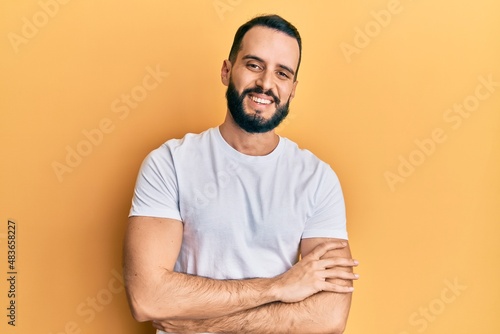 Young man with beard wearing casual white t shirt happy face smiling with crossed arms looking at the camera. positive person. © Krakenimages.com