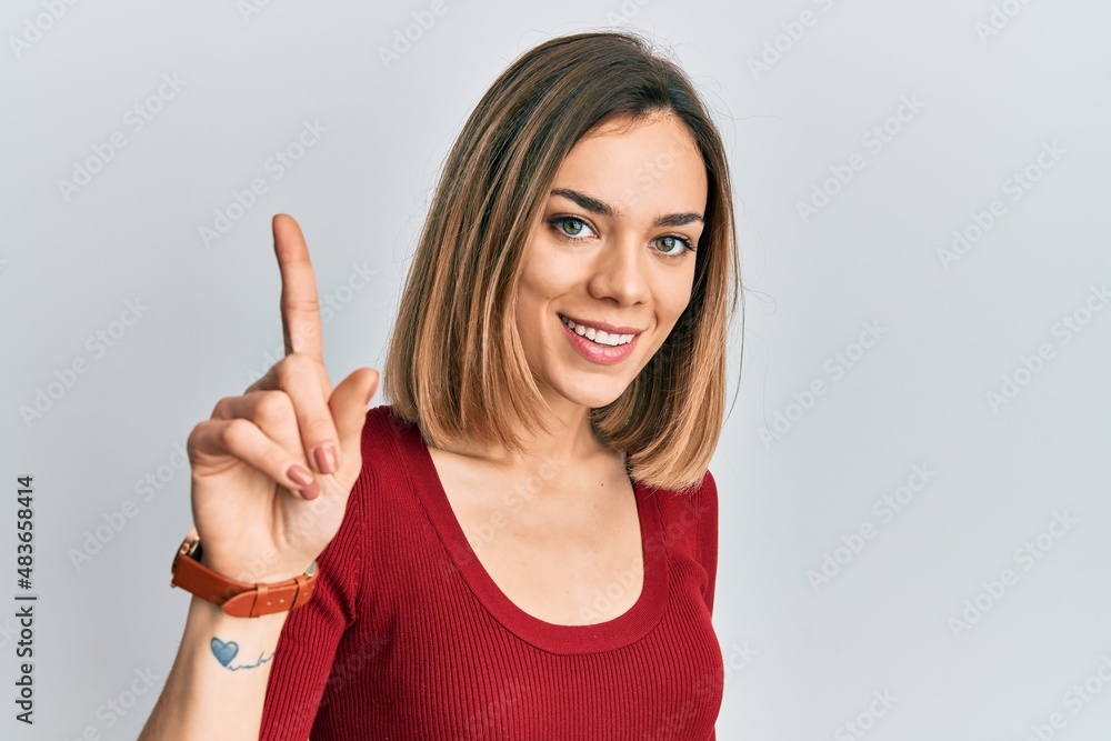 Young caucasian blonde woman wearing casual jumper smiling with an idea or question pointing finger up with happy face, number one Young caucasian blonde woman wearing casual jumper smiling with an idea or question pointing finger up with happy face, number one