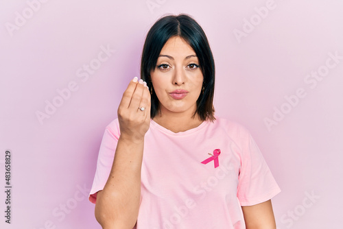 Young hispanic woman wearing pink cancer ribbon on t shirt doing italian gesture with hand and fingers confident expression