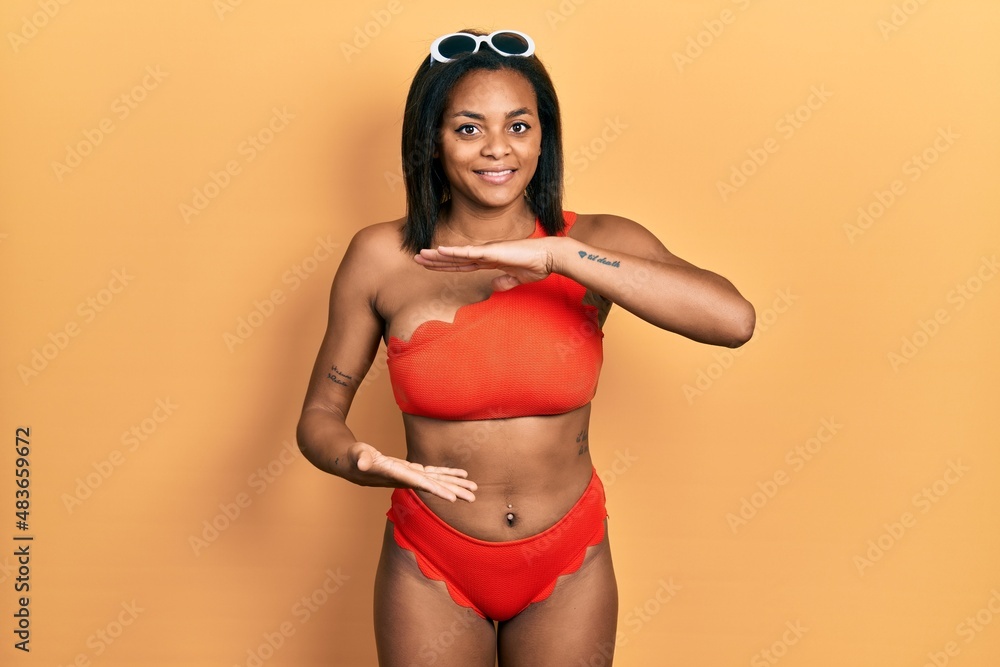 Naklejka premium Young african american girl wearing bikini gesturing with hands showing big and large size sign, measure symbol. smiling looking at the camera. measuring concept.
