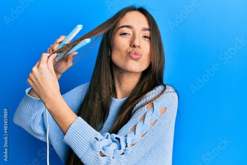 Young hispanic girl holding hair straightener looking at the camera blowing a kiss being lovely and sexy. love expression. photo