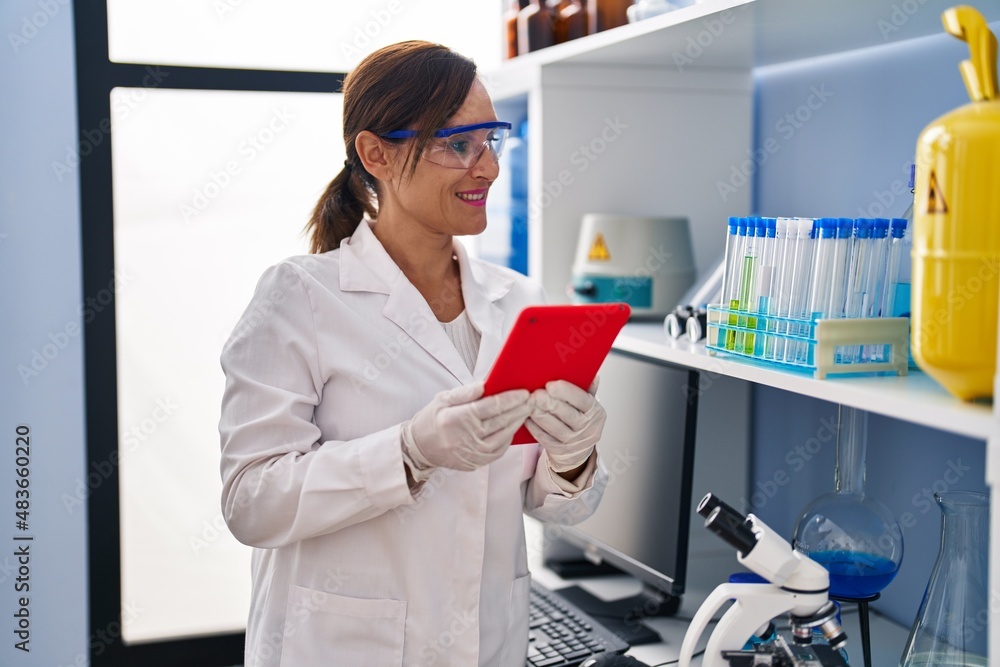 Middle age woman wearing scientist uniform using touchpad at laboratory Middle age woman wearing scientist uniform using touchpad at laboratory