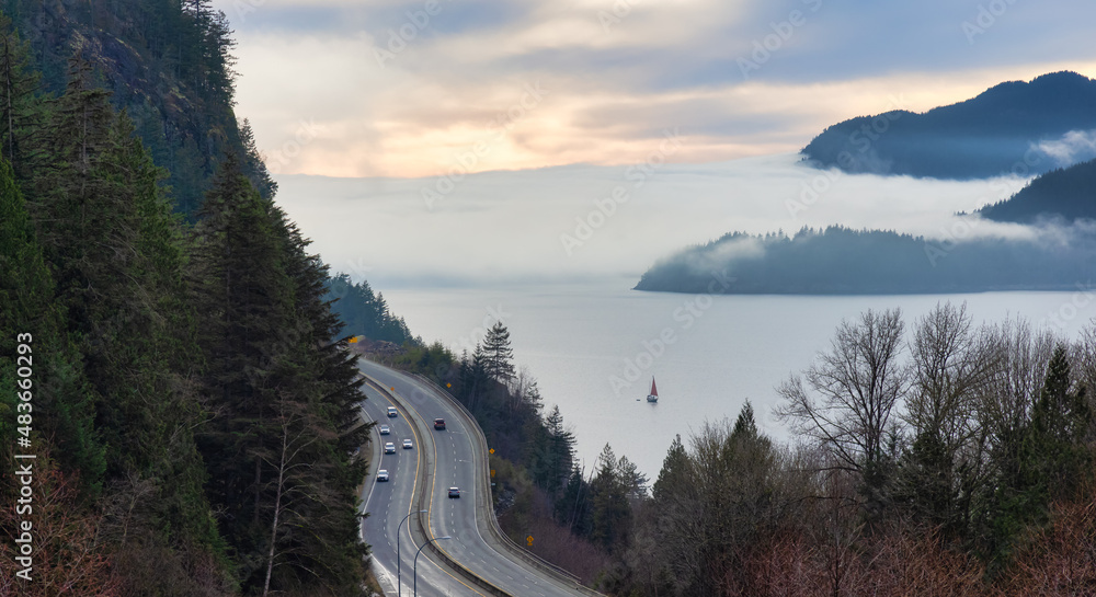 Fototapeta premium Sea to Sky Highway with cars and Howe Sound in background covered in fog and clouds. Winter Sunset Sky. Porteau Cove Road Lookout near Vancouver and Squamish, BC, Canada.