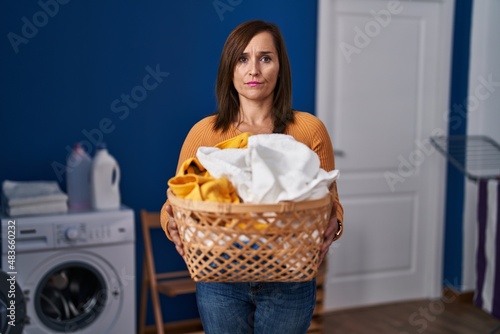 Middle age woman holding laundry basket at laundry room skeptic and nervous, frowning upset because of problem. negative person.