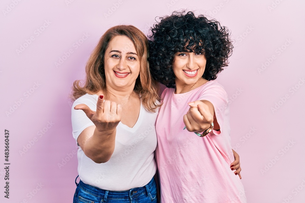 Middle east mother and daughter wearing casual clothes beckoning come here gesture with hand inviting welcoming happy and smiling