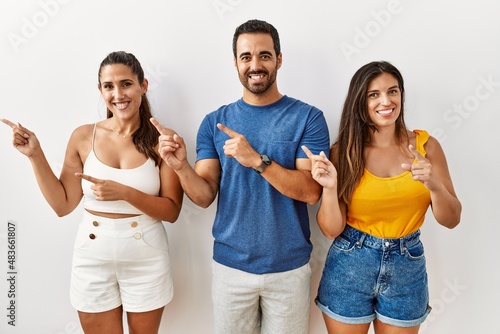 Group of young hispanic people standing over isolated background smiling and looking at the camera pointing with two hands and fingers to the side.