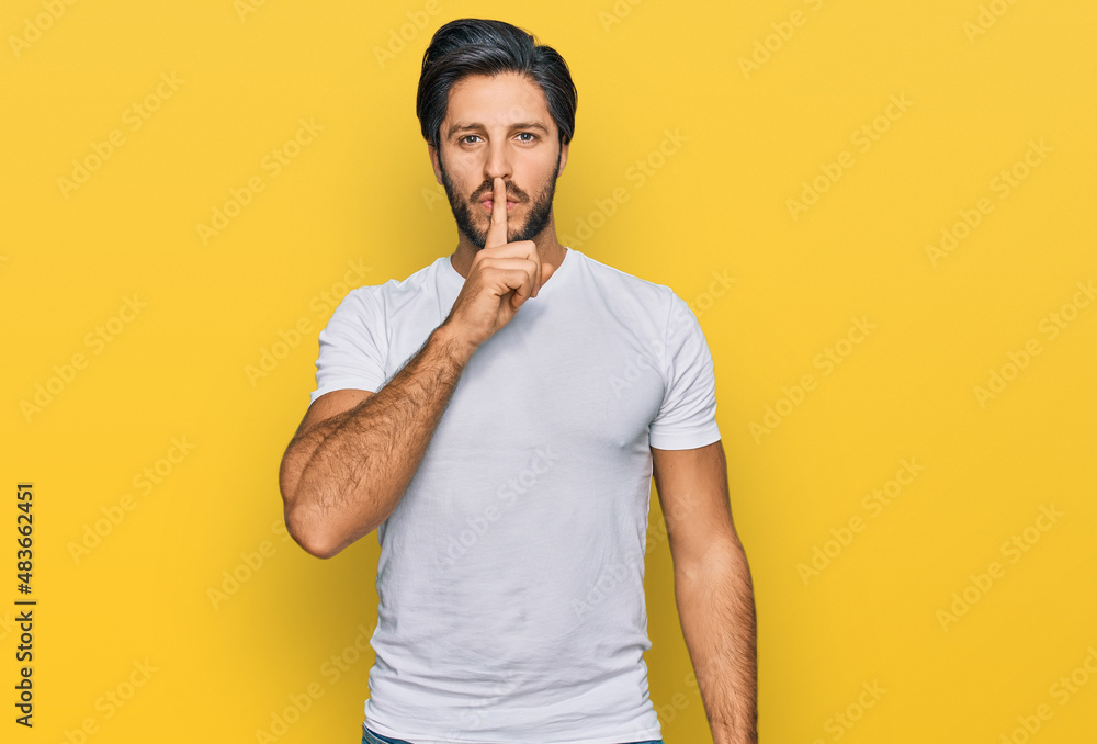 Young hispanic man wearing casual white t shirt asking to be quiet with finger on lips. silence and secret concept. Young hispanic man wearing casual white t shirt asking to be quiet with finger on lips. silence and secret concept.