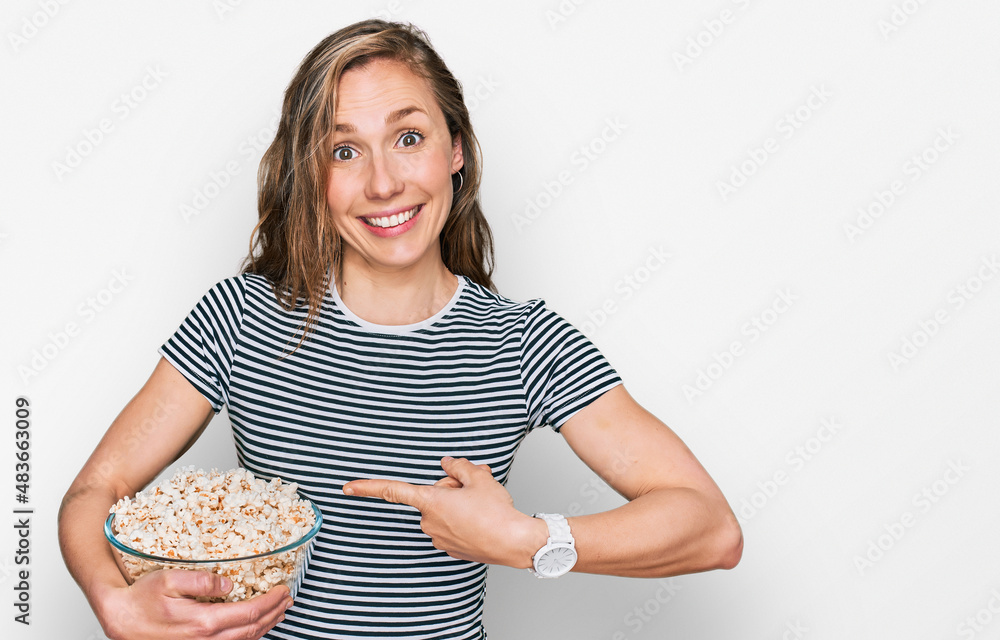 Young blonde woman eating popcorn smiling happy pointing with hand and finger Young blonde woman eating popcorn smiling happy pointing with hand and finger