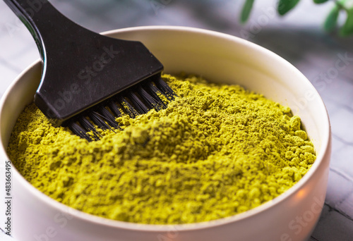 Green natural henna powder in bowl with black brush