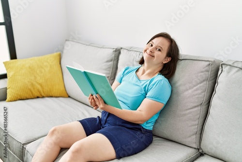 Brunette woman with down syndrome sitting on the sofa reading a book at the living room