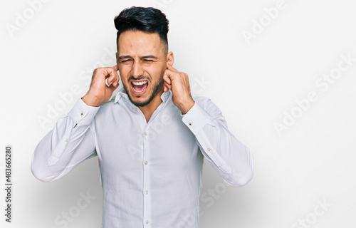 Young arab man wearing casual clothes covering ears with fingers with annoyed expression for the noise of loud music. deaf concept.