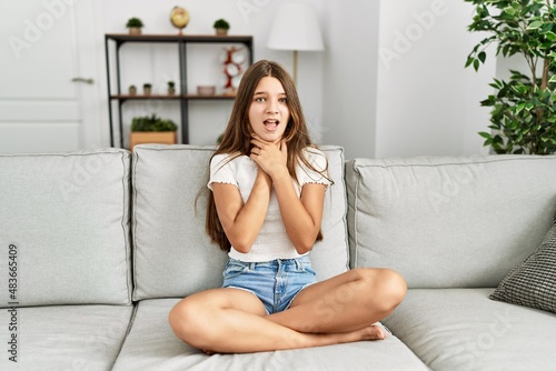 Young brunette teenager sitting on the sofa at home shouting and suffocate because painful strangle. health problem. asphyxiate and suicide concept.