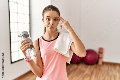 Young brunette teenager wearing sportswear holding water bottle shooting and killing oneself pointing hand and fingers to head like gun, suicide gesture.