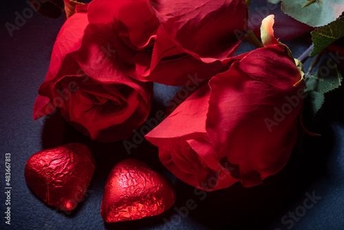 Fototapeta Naklejka Na Ścianę i Meble -  Closeup of heart shaped chocolate confections, red roses and a gift against dark background.