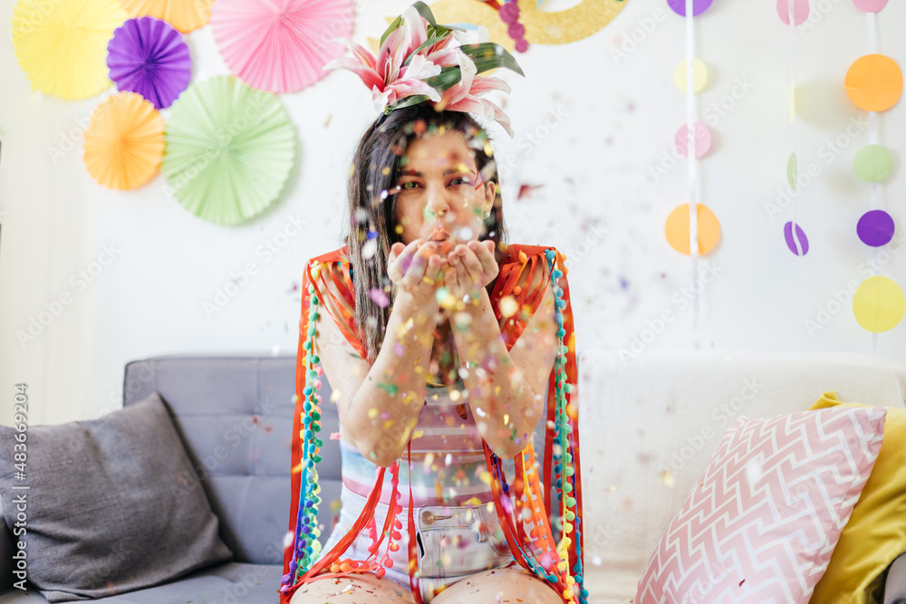 Brazilian Carnival. Young woman enjoying the carnival at home blowing confetti