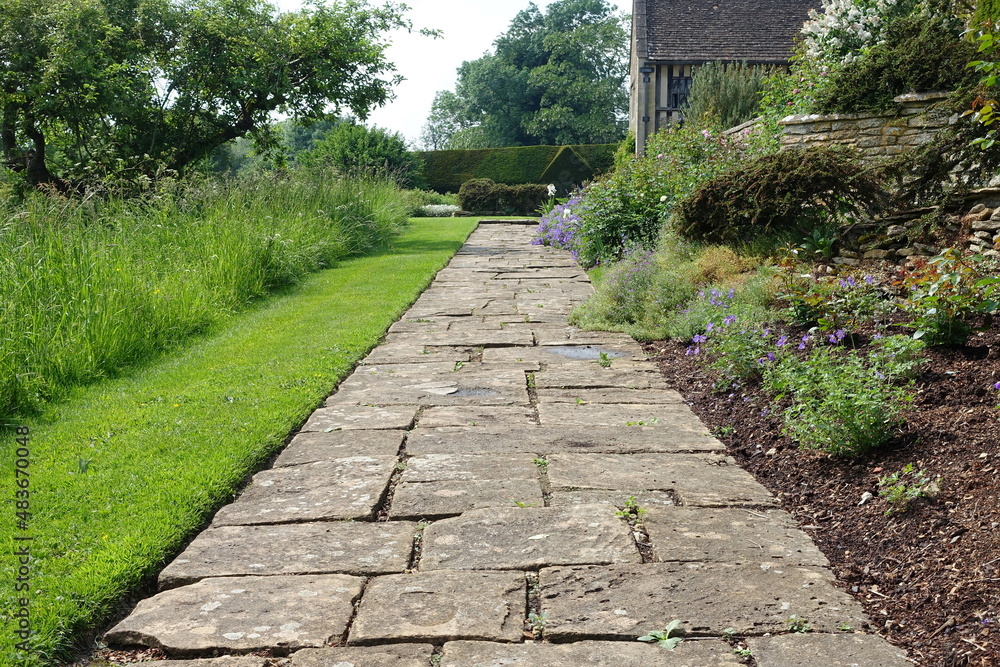 Scenic View of a Stone Path Way Lined by Plants and Flowers in a Beautiful English Style Formal Garden Scenic View of a Stone Path Way Lined by Plants and Flowers in a Beautiful English Style Formal Garden